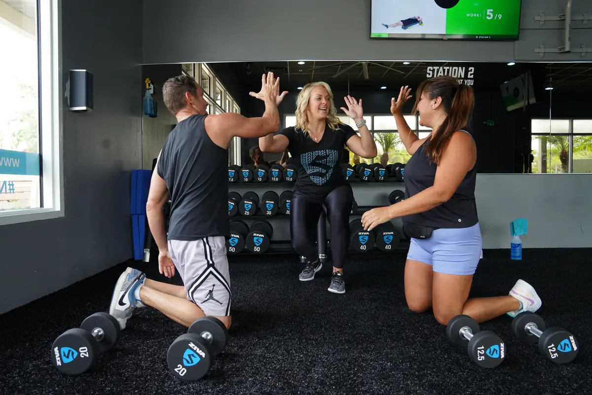 SWEAT440 members kneeling beside their dumbbells and high-fiving during a group strength class