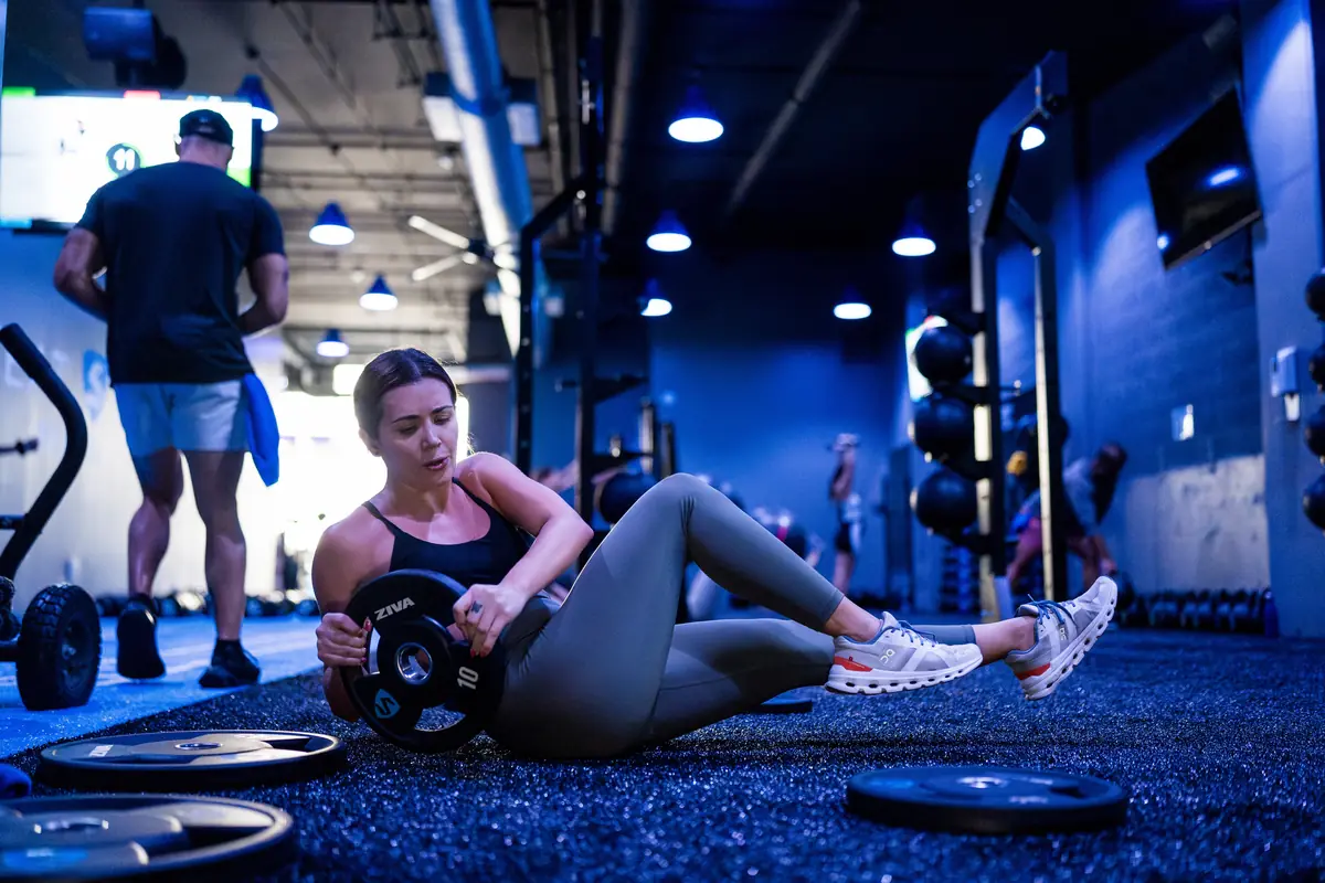 Woman doing a weighted core rotation with a plate on the gym floor