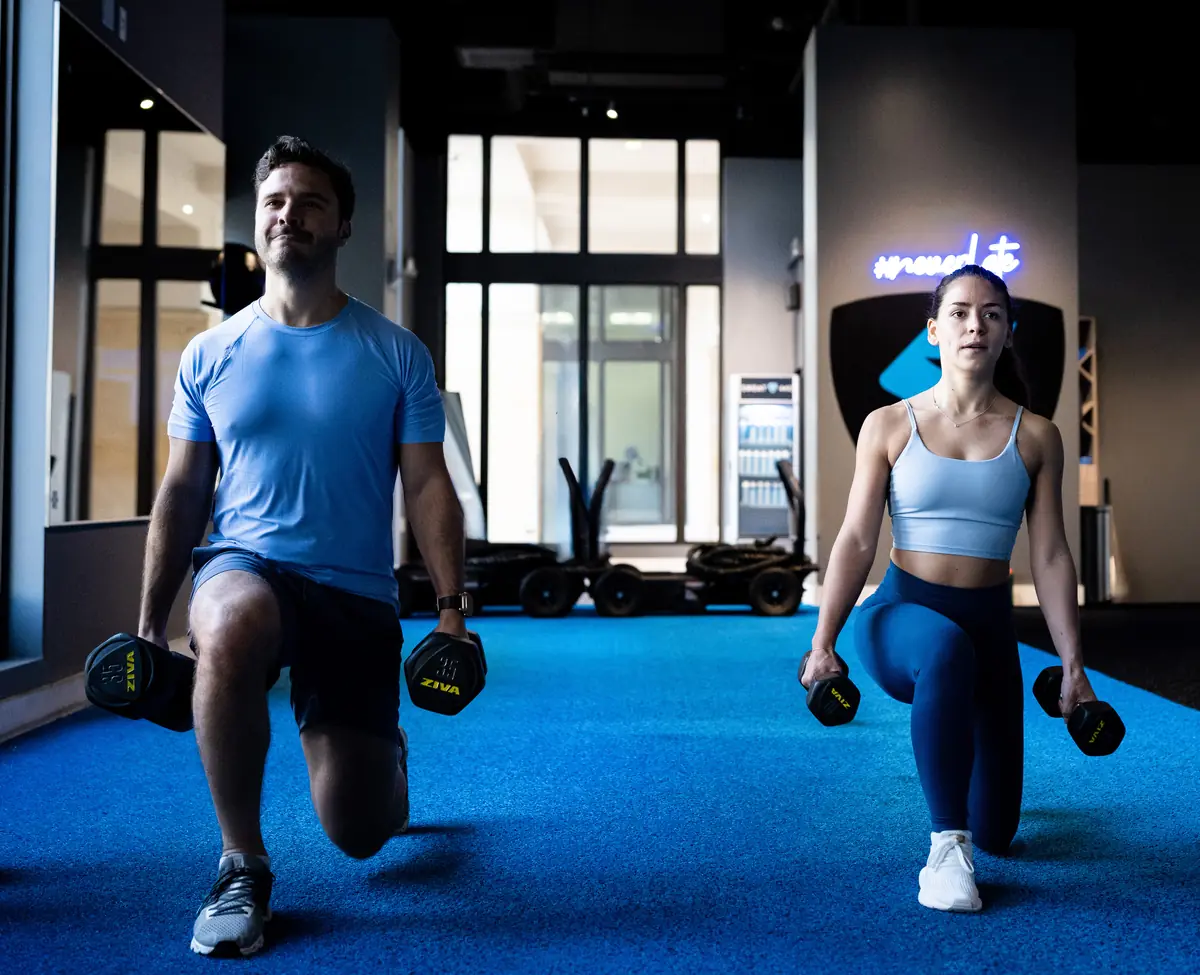 Man and woman doing dumbbell lunges during a SWEAT440 strength class