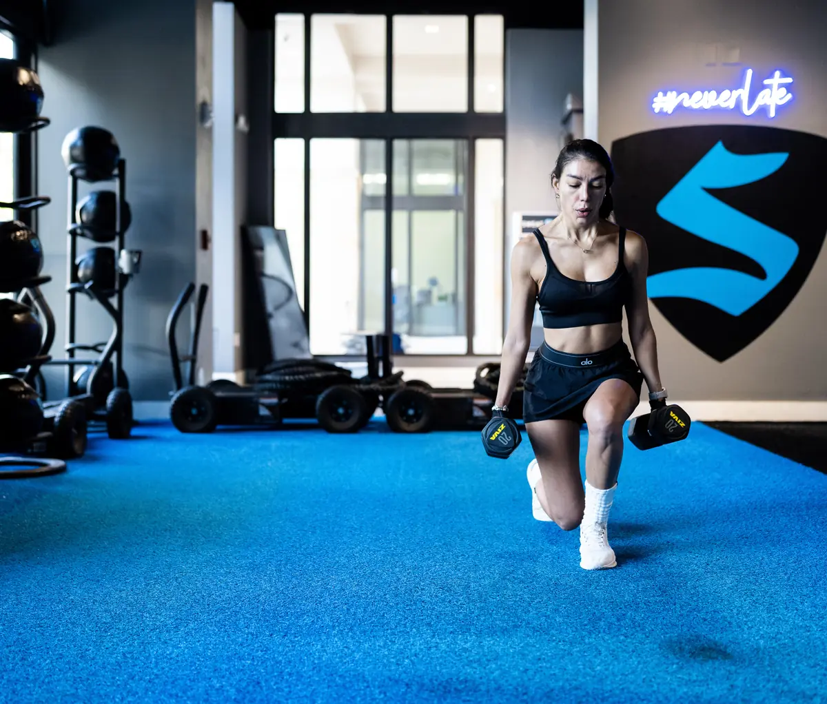 Woman doing a dumbbell reverse lunge at SWEAT440