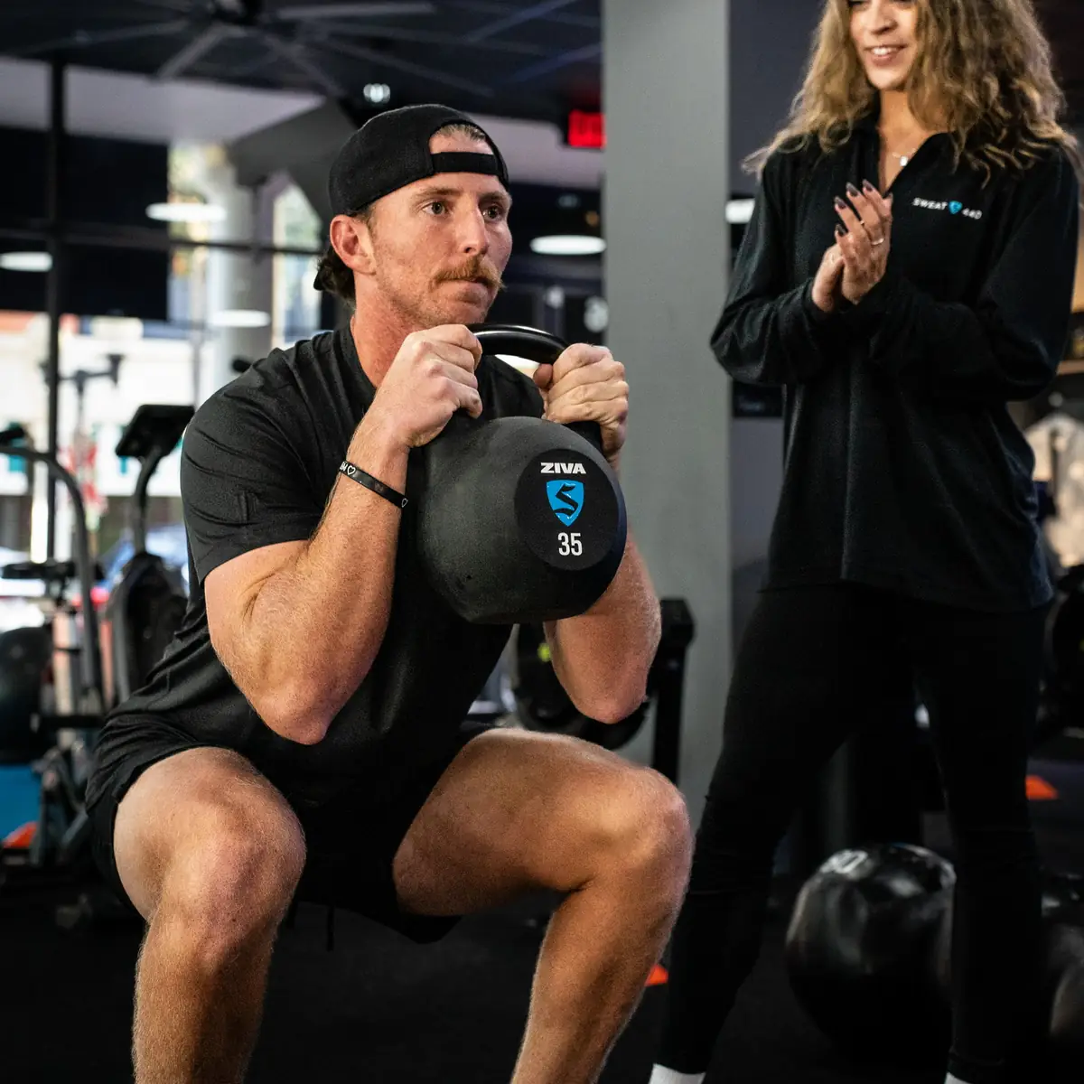 SWEAT440 coach cheering on a member doing a kettlebell goblet squat