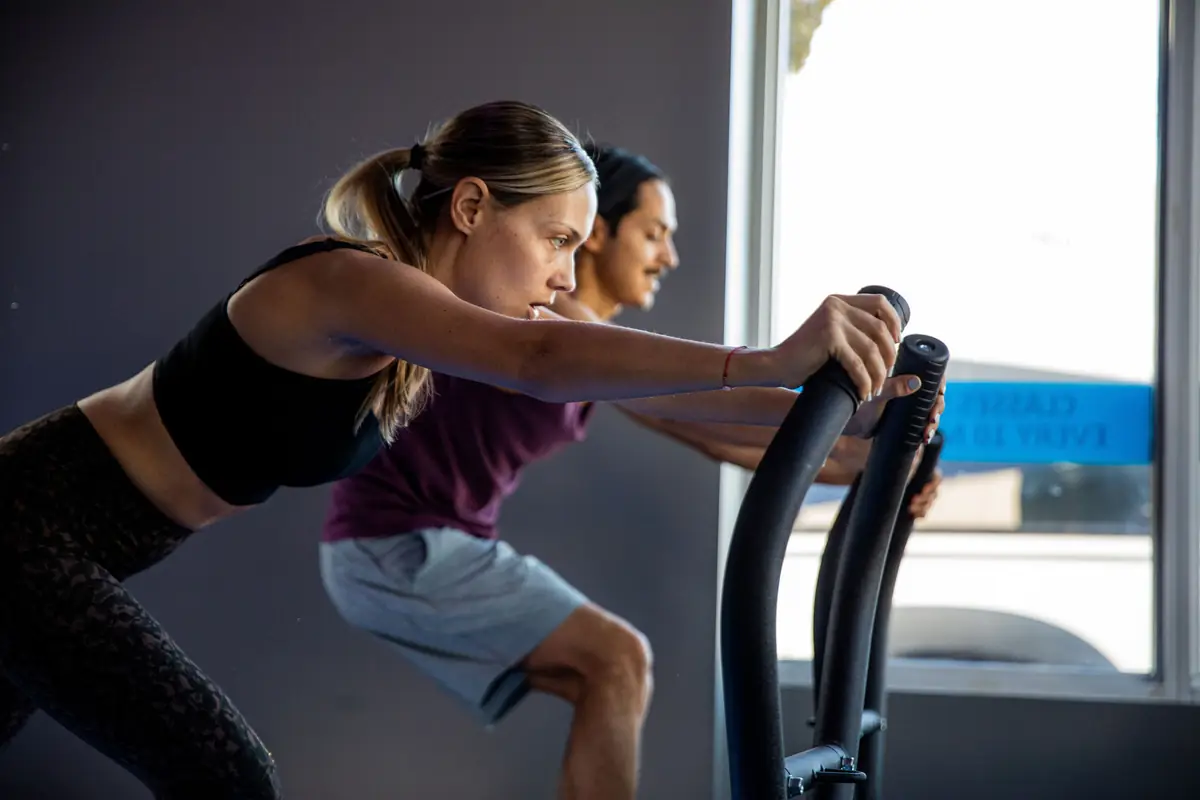 Two SWEAT440 members pushing hard on air bikes during a cardio station
