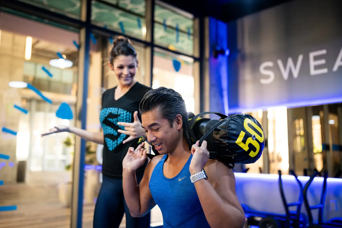 SWEAT440 coach encouraging a member carrying a 50-pound sandbag