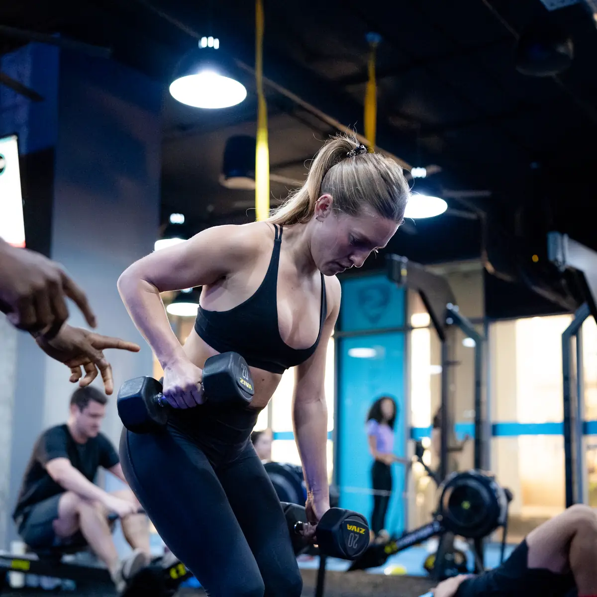 Woman doing a bent-over dumbbell row while a SWEAT440 coach points out her form