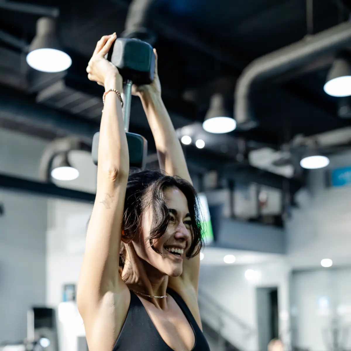 Woman pressing a dumbbell overhead during a SWEAT440 strength class