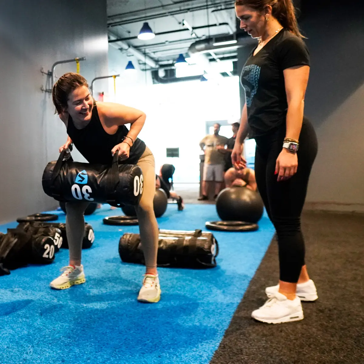 SWEAT440 coach guiding a member through a sandbag lift