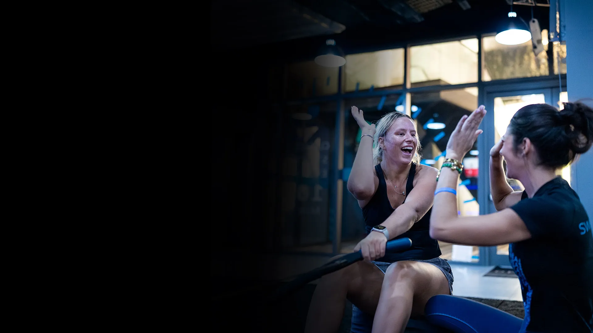 SWEAT440 member on a rower high-fiving a coach inside a SWEAT440 franchise studio